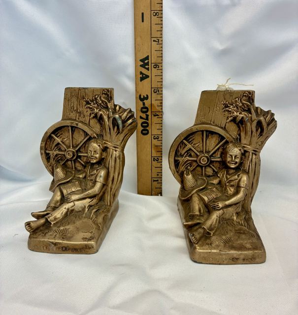 Pair of cast metal bookends of a boy reading by a wagon wheel